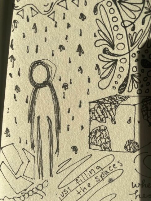 A doodle of a faceless human figure standing among lines and rain-like drops, surrounded by abstract shapes and handwritten text on paper.