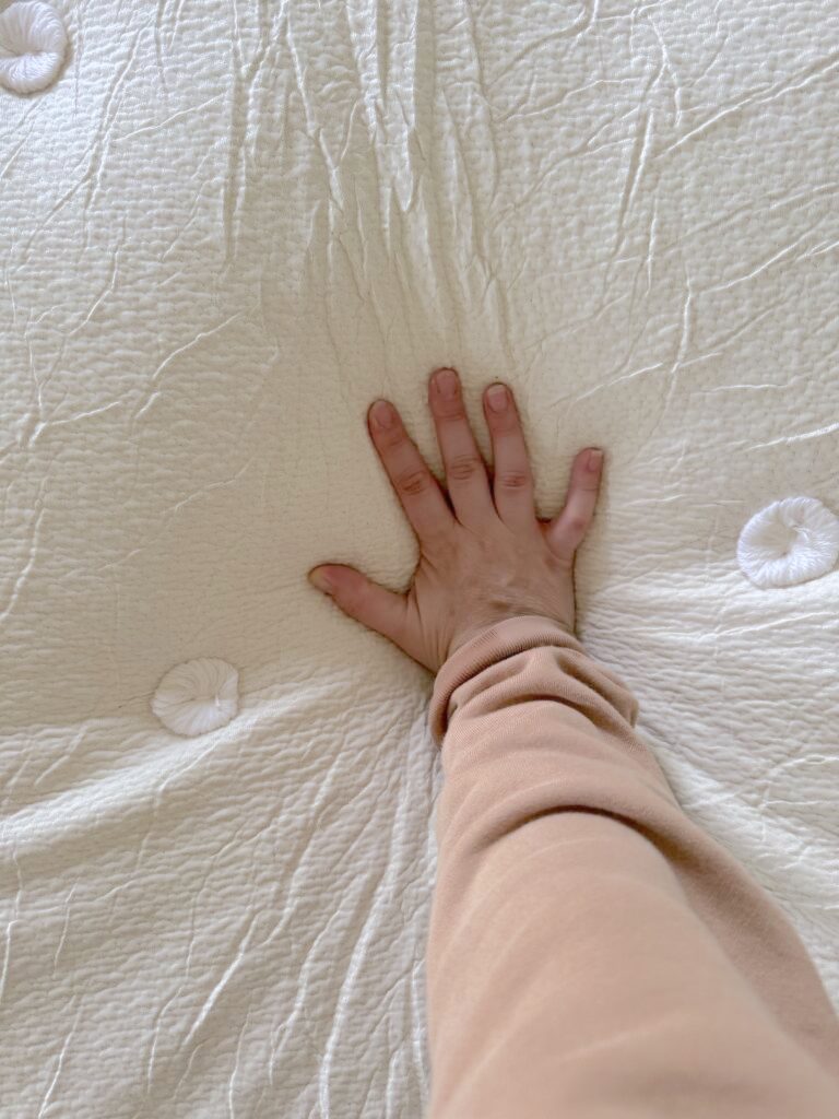 Reviewer Kayti Christian's hand presses down on the nontoxic Avocado mattress, creating an indentation in its textured surface.