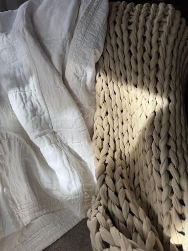 A textured, woven blanket and a white quilt are placed side by side, with sunlight creating shadows on the surfaces.