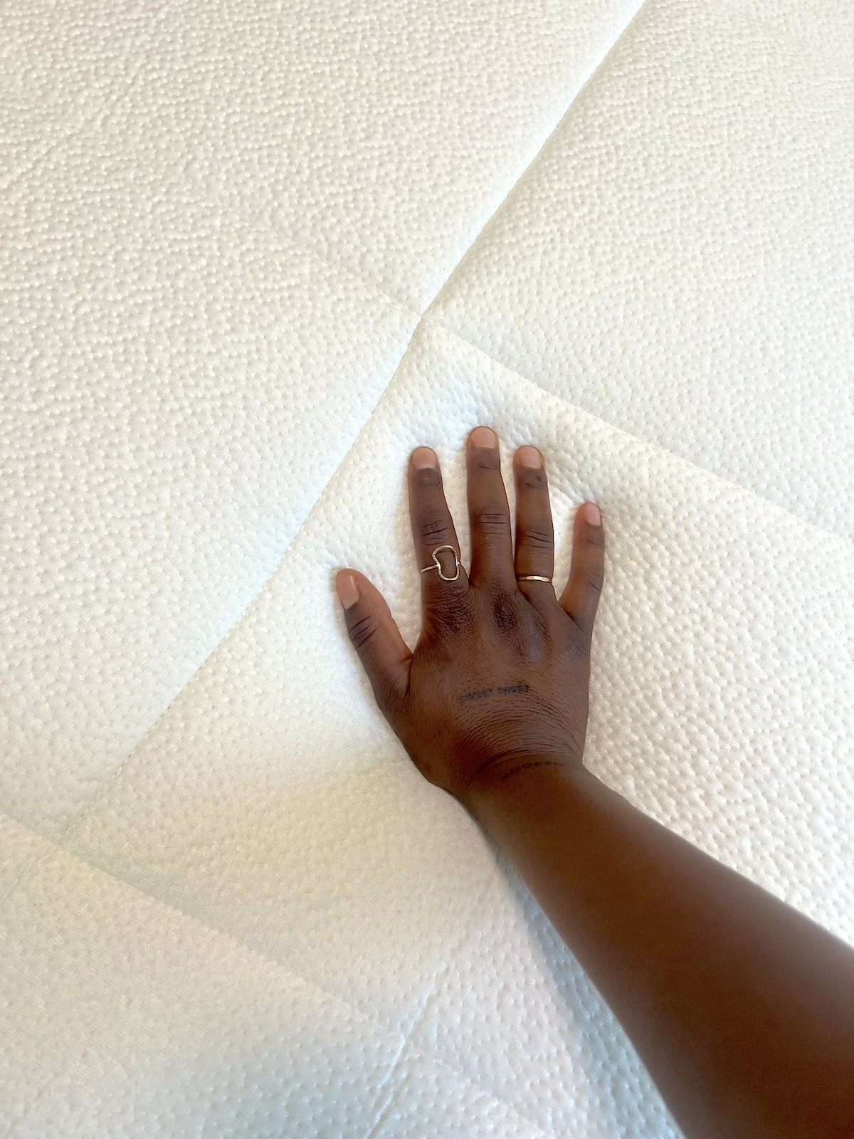 Langa Chinyoka's hand presses down on a white Awara mattress, demonstrating its flexibility. This organic mattress offers a nontoxic sleeping environment for peace of mind and comfort.