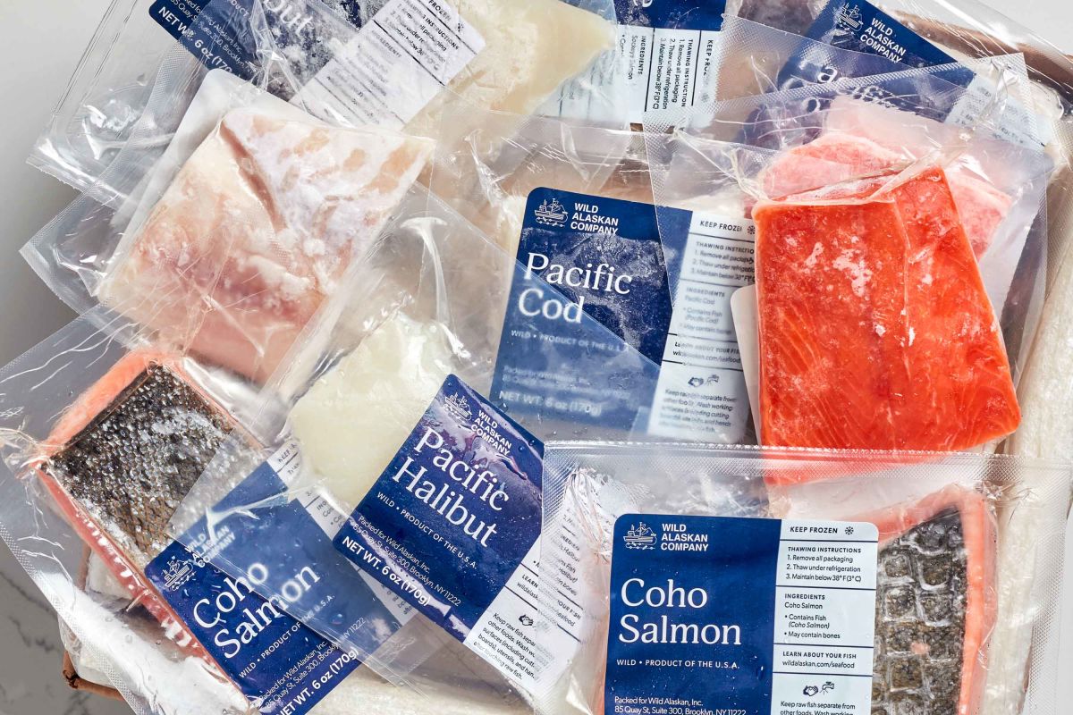 A variety of vacuum-sealed fish packages include Pacific Cod, Coho Salmon, and Halibut, all with labeled packaging from the Wild Alaskan Company on a white surface.