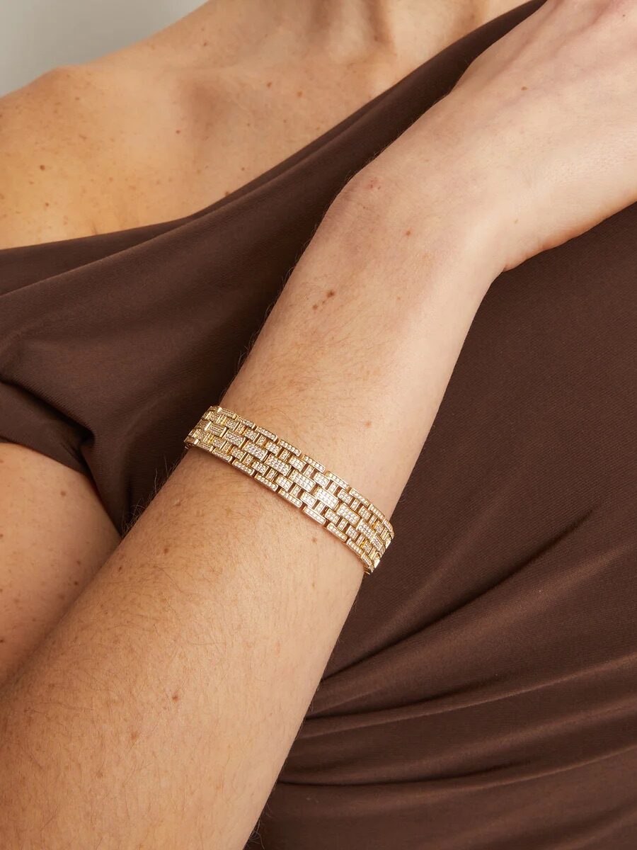 A person wearing a gold link bracelet on their wrist, dressed in an off-shoulder brown top.