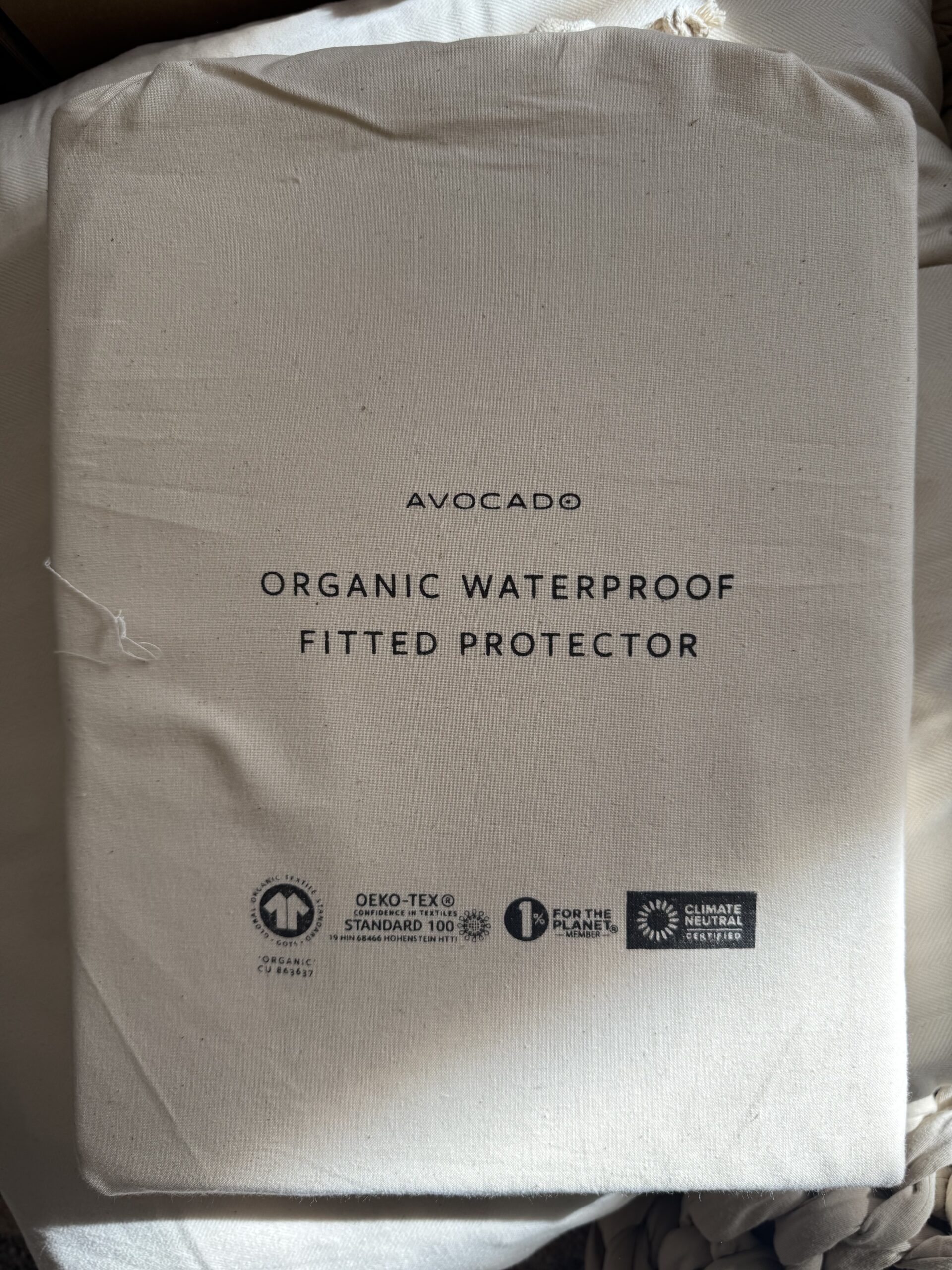 Packaging of an Avocado brand organic waterproof fitted protector, with certification logos displayed at the bottom.