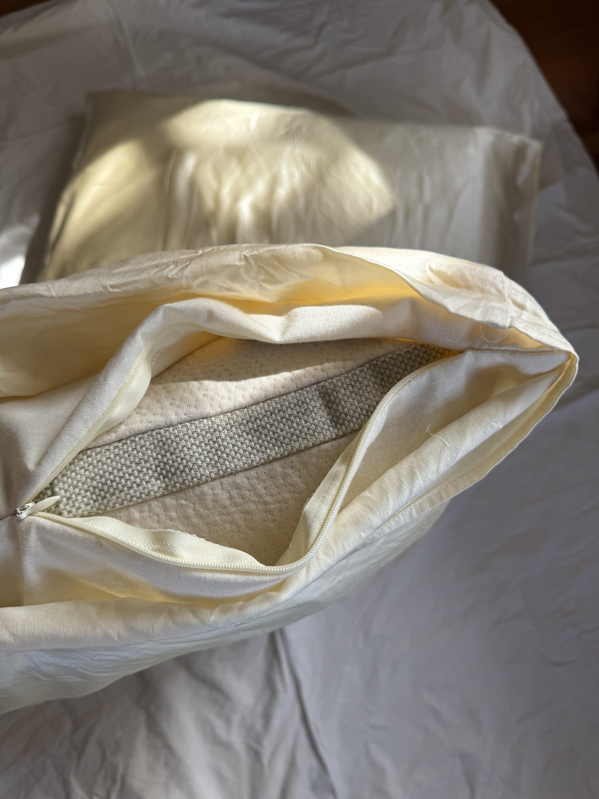Pillow partially unzipped, revealing a white foam interior, on a crumpled white sheet background.