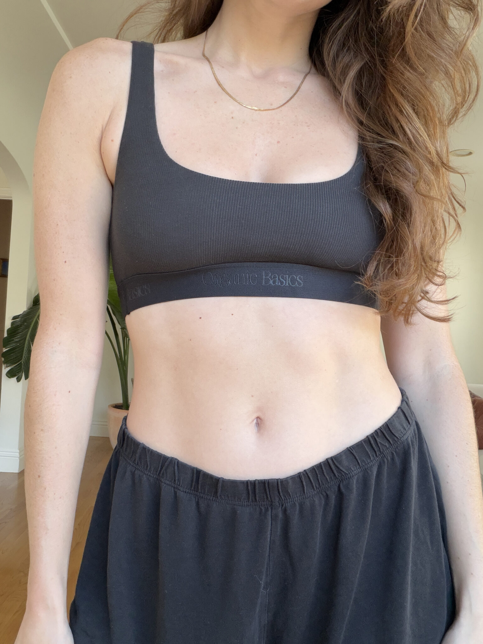 A woman wearing a black sports bra and black pants stands indoors, partially facing the camera.