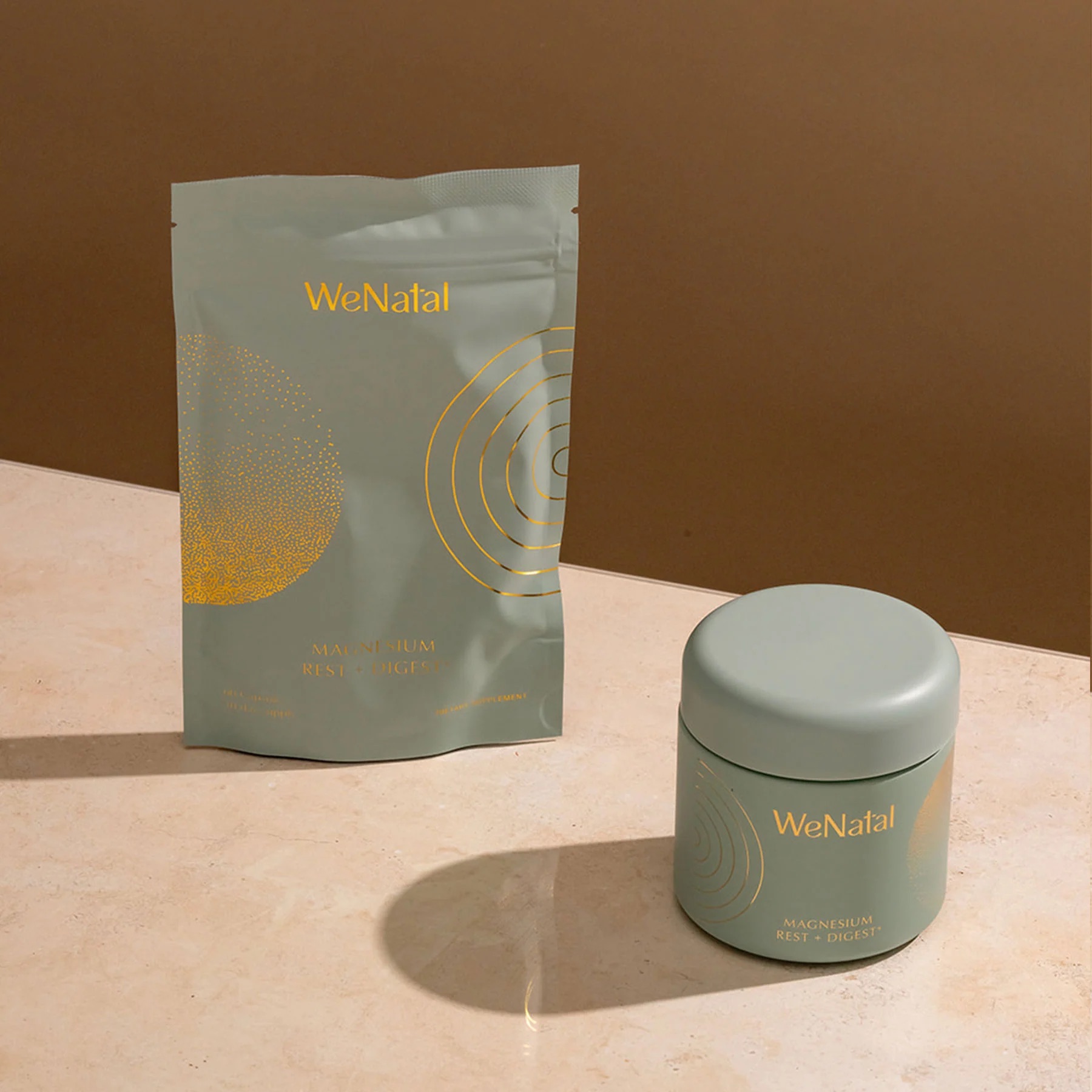 A light green pouch and matching jar labeled "WeNatal Magnesium Rest & Digest" on a beige surface with a brown background.