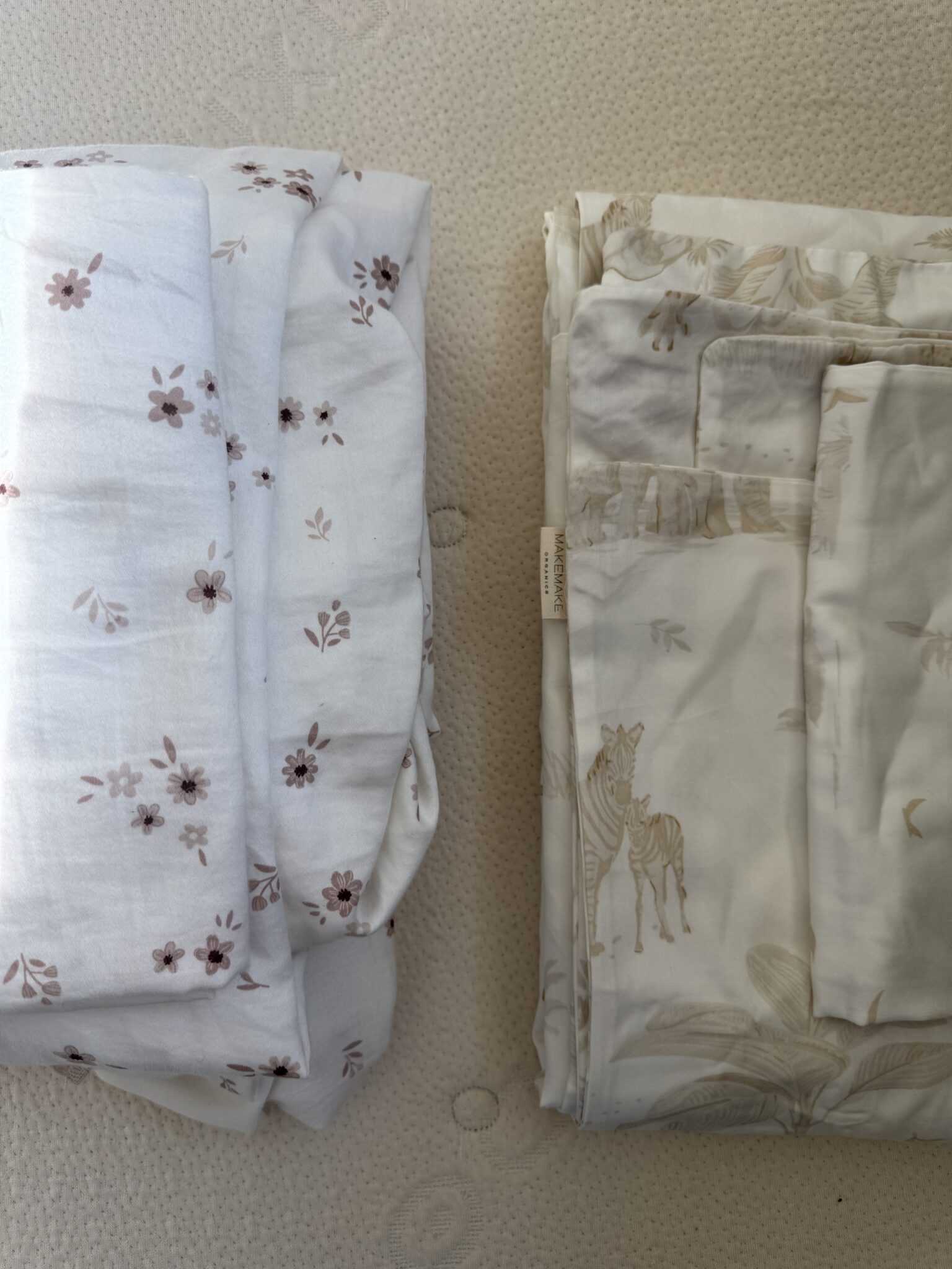 Two folded stacks of bed sheets on a textured surface; the left has a small brown floral pattern, the right features a light animal and plant design.