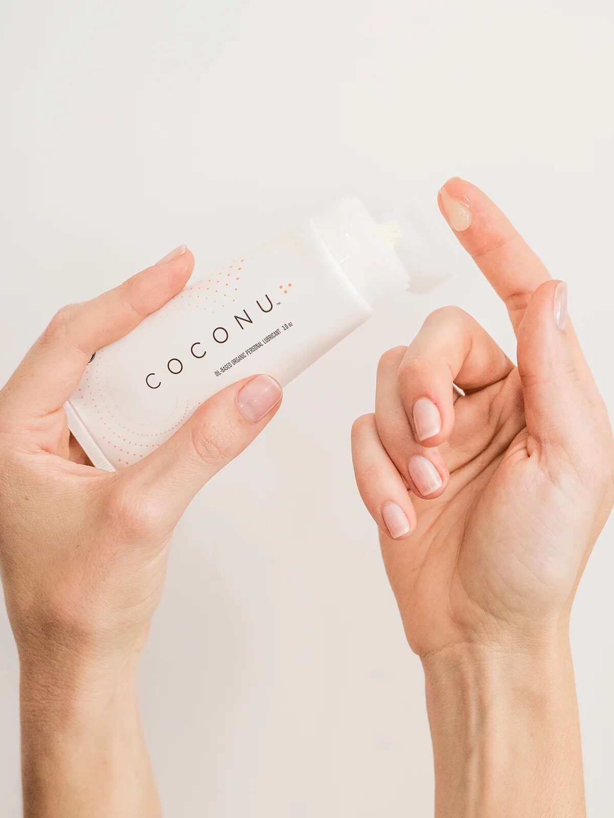 A person dispenses a small amount of Coconu product onto their fingertip from a white bottle.