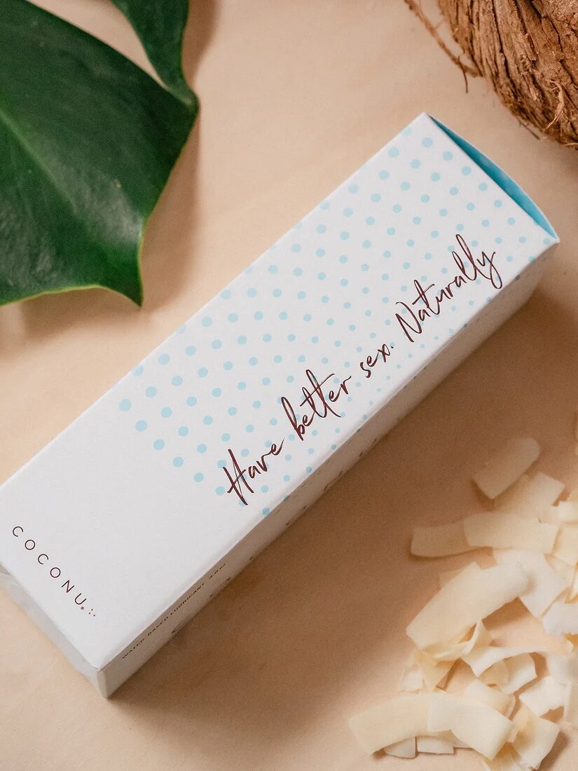 Rectangular box labeled "Have better sex. Naturally." sits on a beige surface surrounded by coconut pieces and a green leaf.