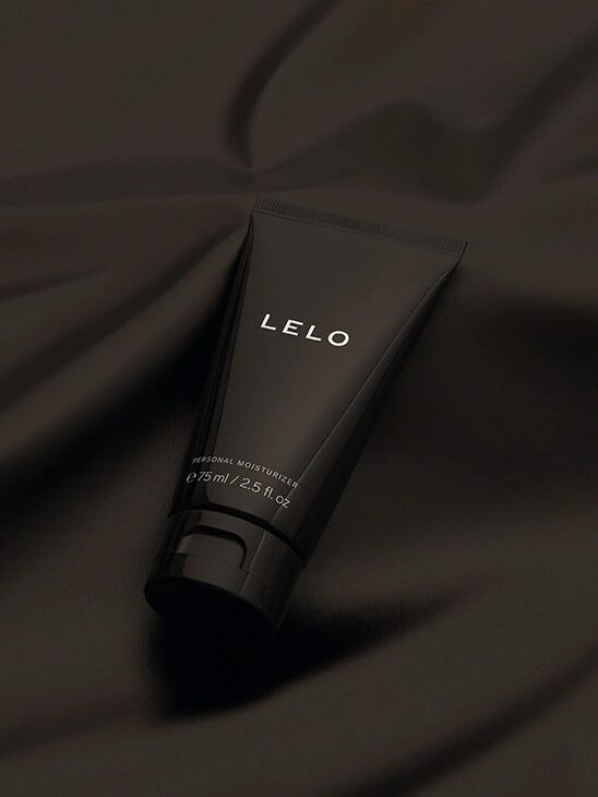 A black tube labeled "LELO" rests on dark, silky fabric. The tube appears to contain personal moisturizer, with a capacity of 2.5 fl. oz.