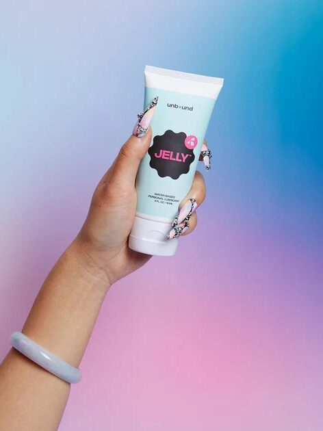 A hand with painted nails holds a tube labeled “Jelly” against a pastel gradient background.