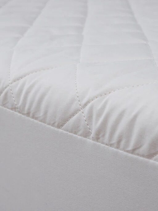 Close-up of a white quilted mattress corner with a textured surface and a fabric border.