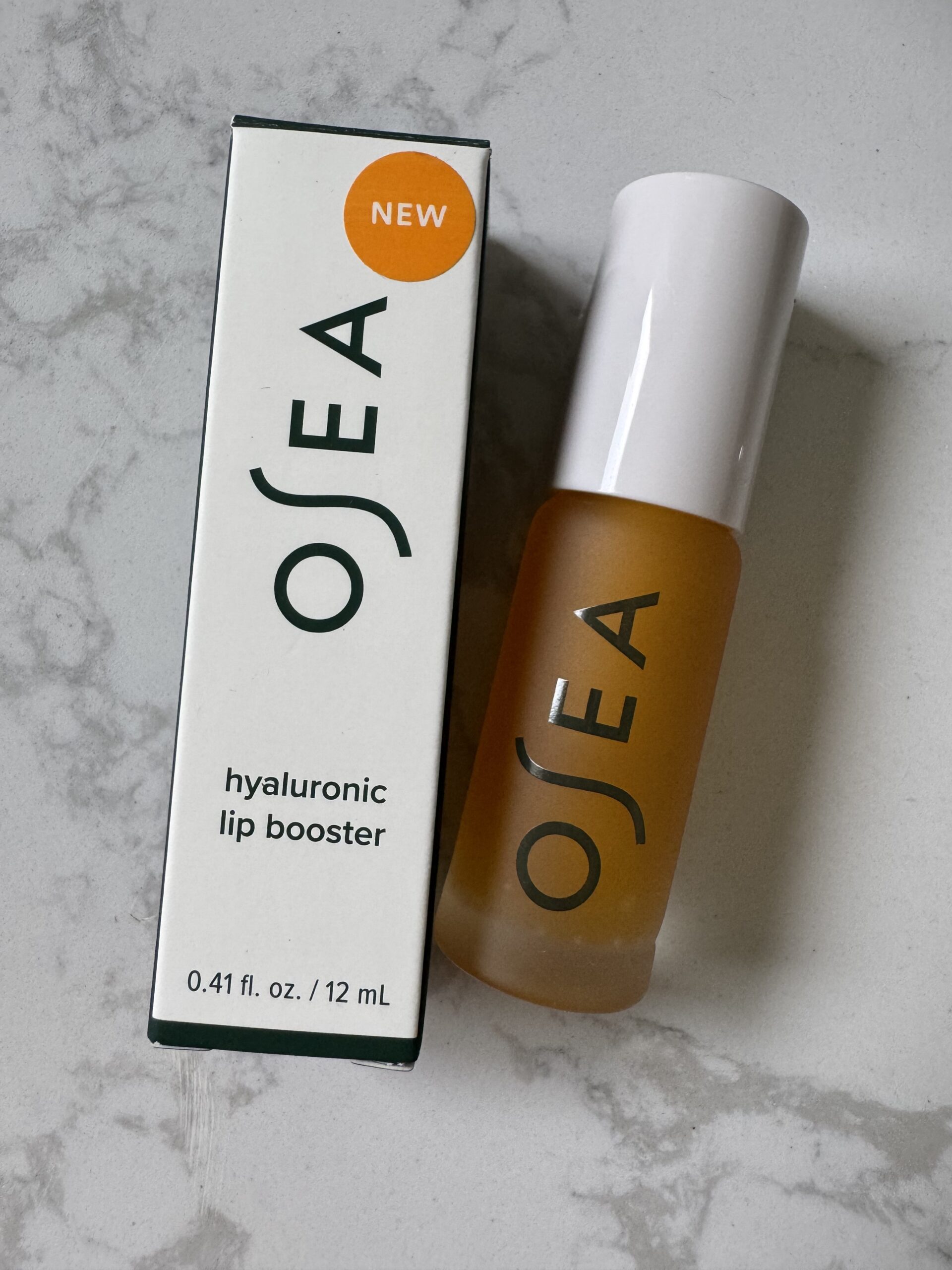 OSEA hyaluronic lip booster product with box and bottle displayed on a light marble surface.