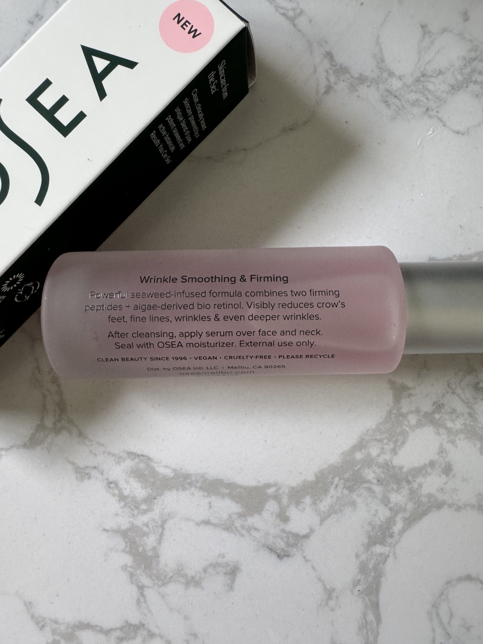 A pink bottle labeled "Wrinkle Smoothing & Firming" serum lies on a marble surface next to a partially visible OSEA product box.