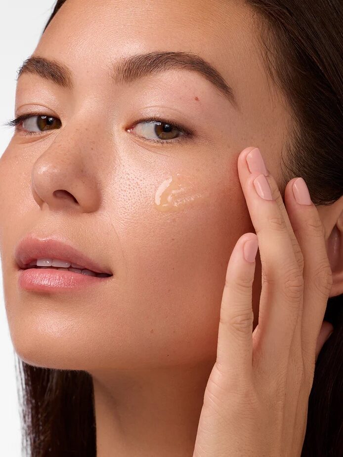 A woman applies a skincare product to her cheek with her fingers.