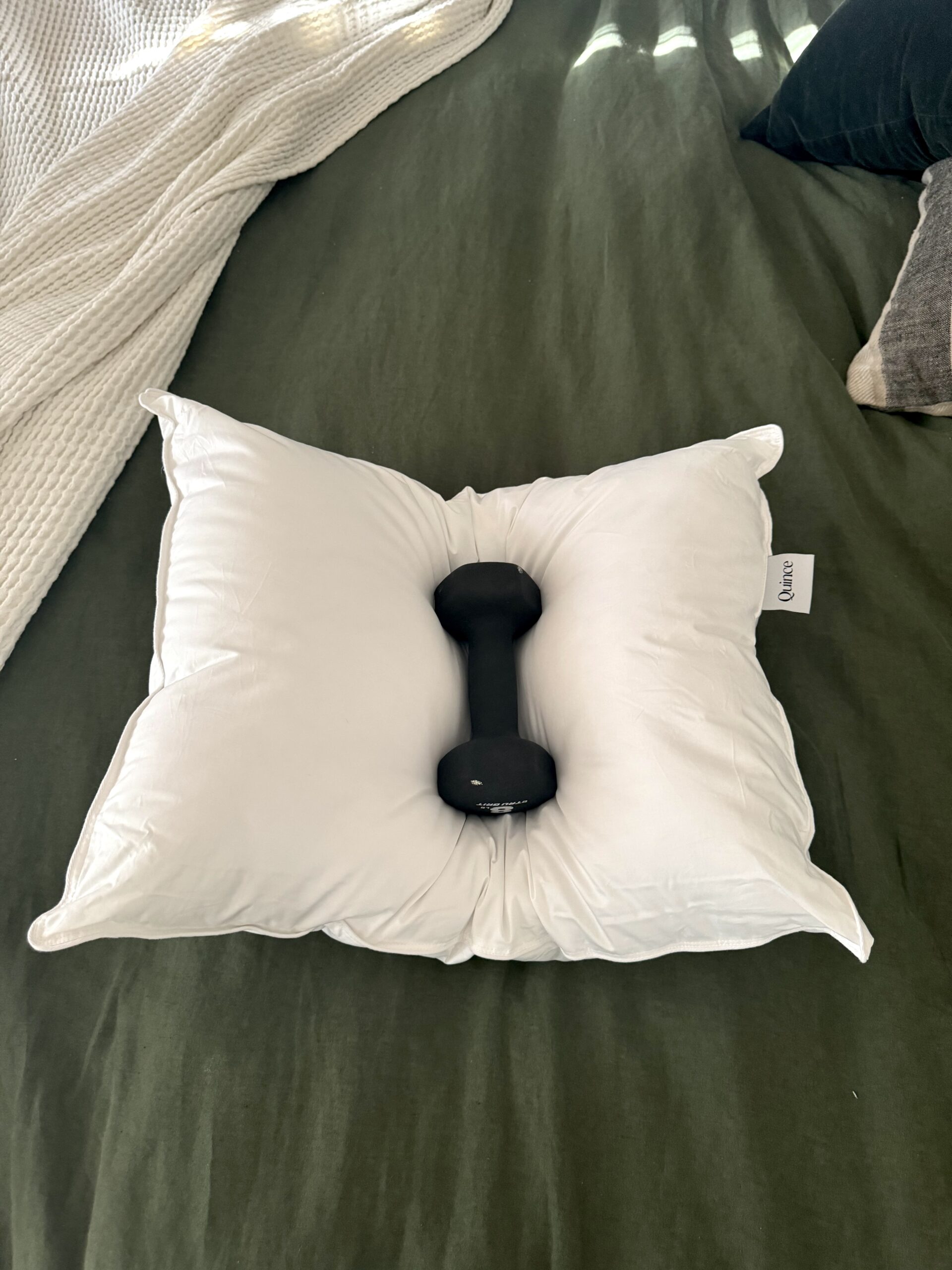A white pillow with a small black dumbbell placed on top lies on a green bedspread.