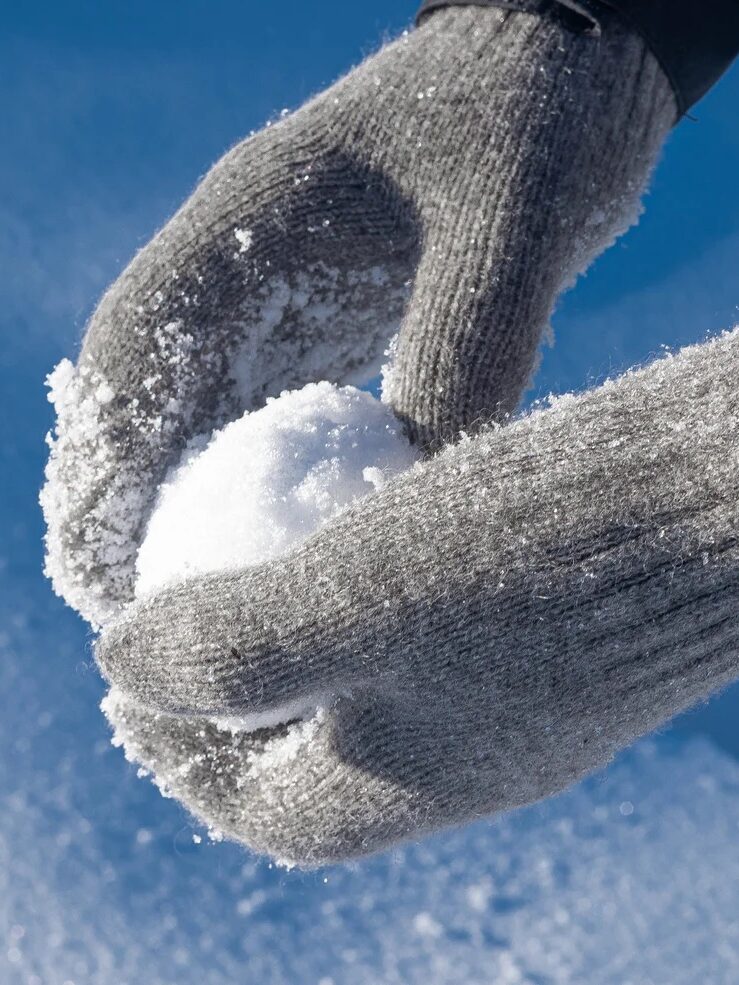 Person wearing gray gloves making a snowball in bright sunlight.