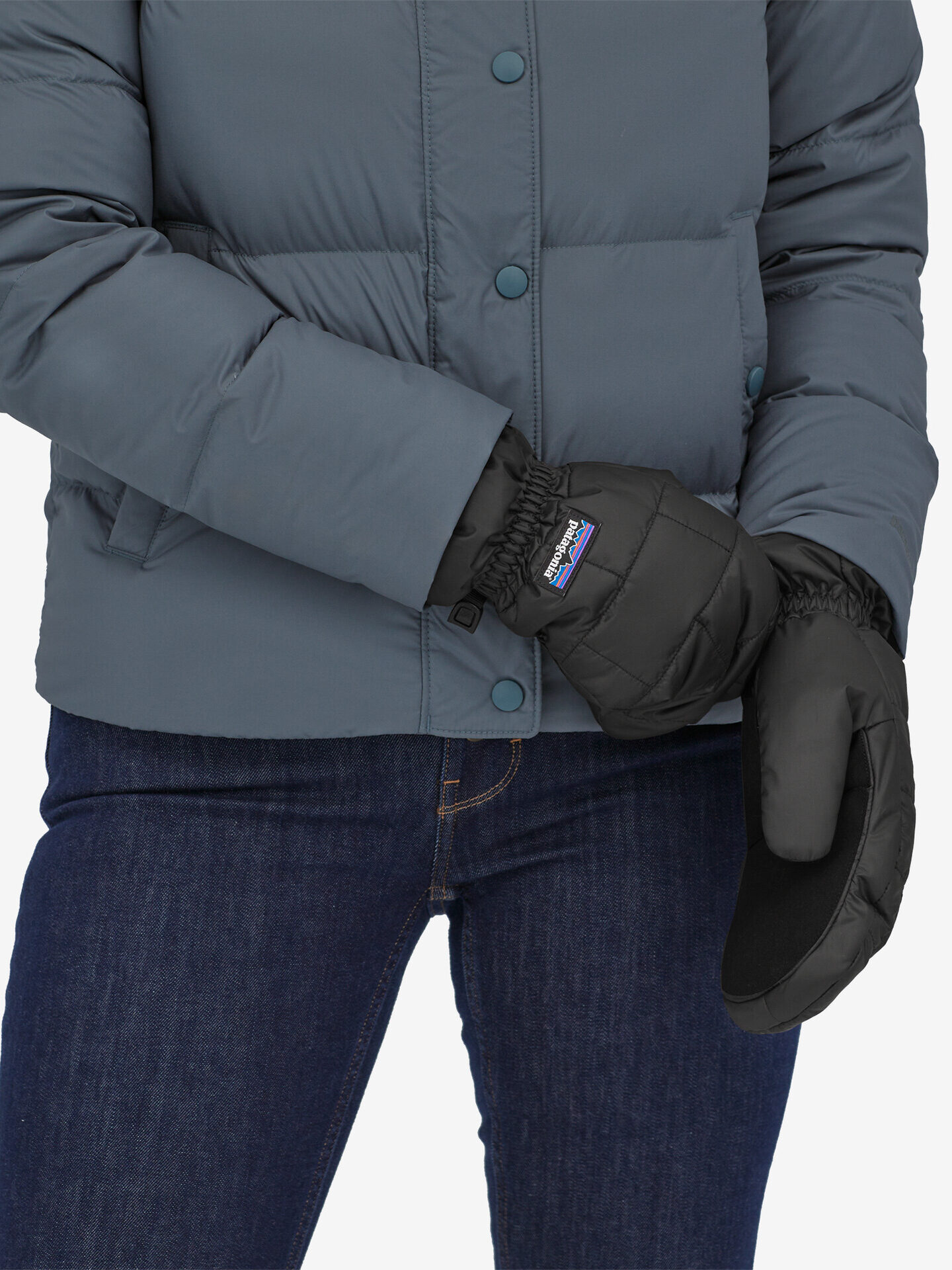 Person in a blue puffer jacket and jeans putting on black mittens.