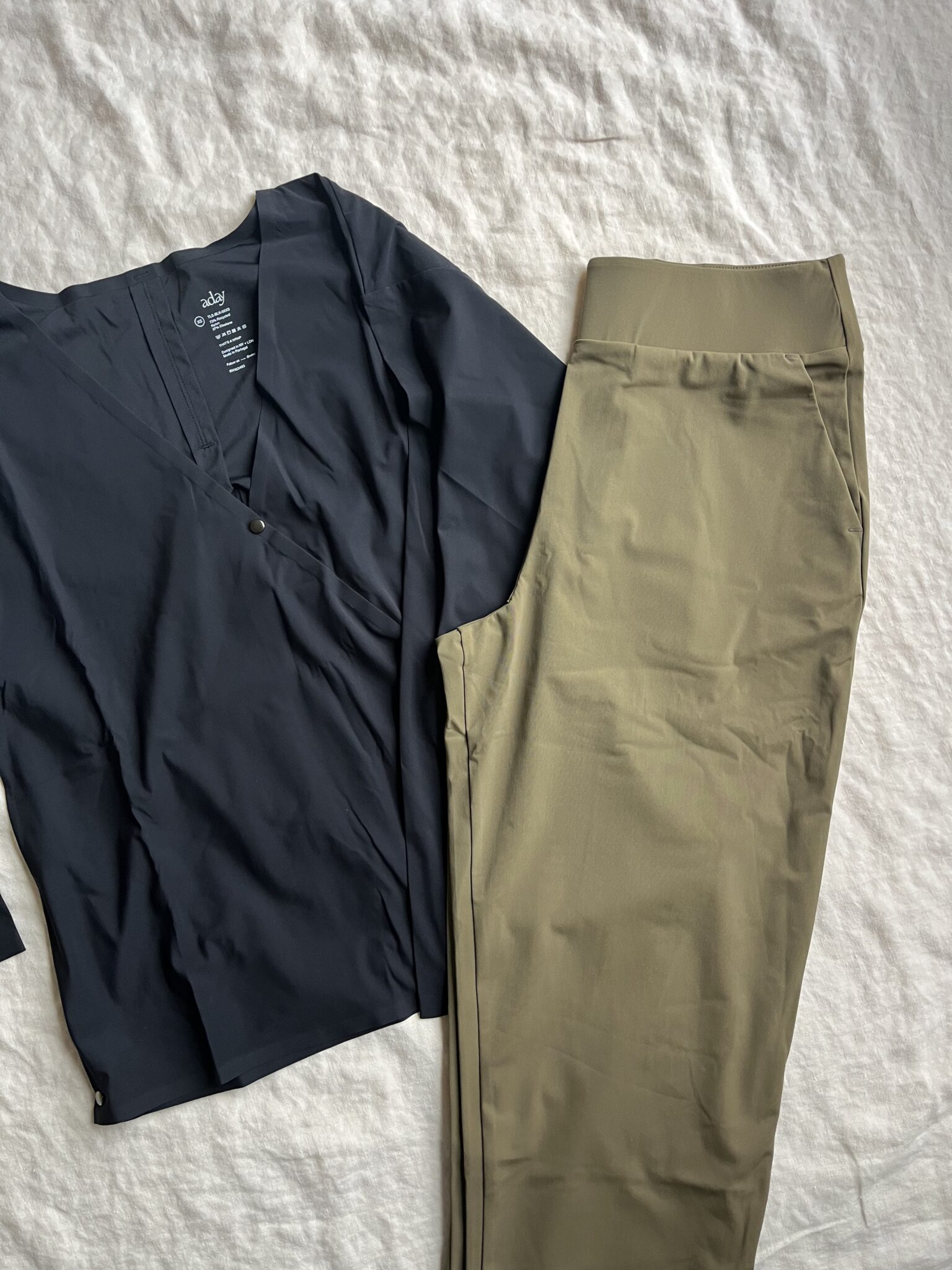 A navy blue long-sleeve shirt and a pair of olive green pants are laid out side by side on a light-colored fabric background.