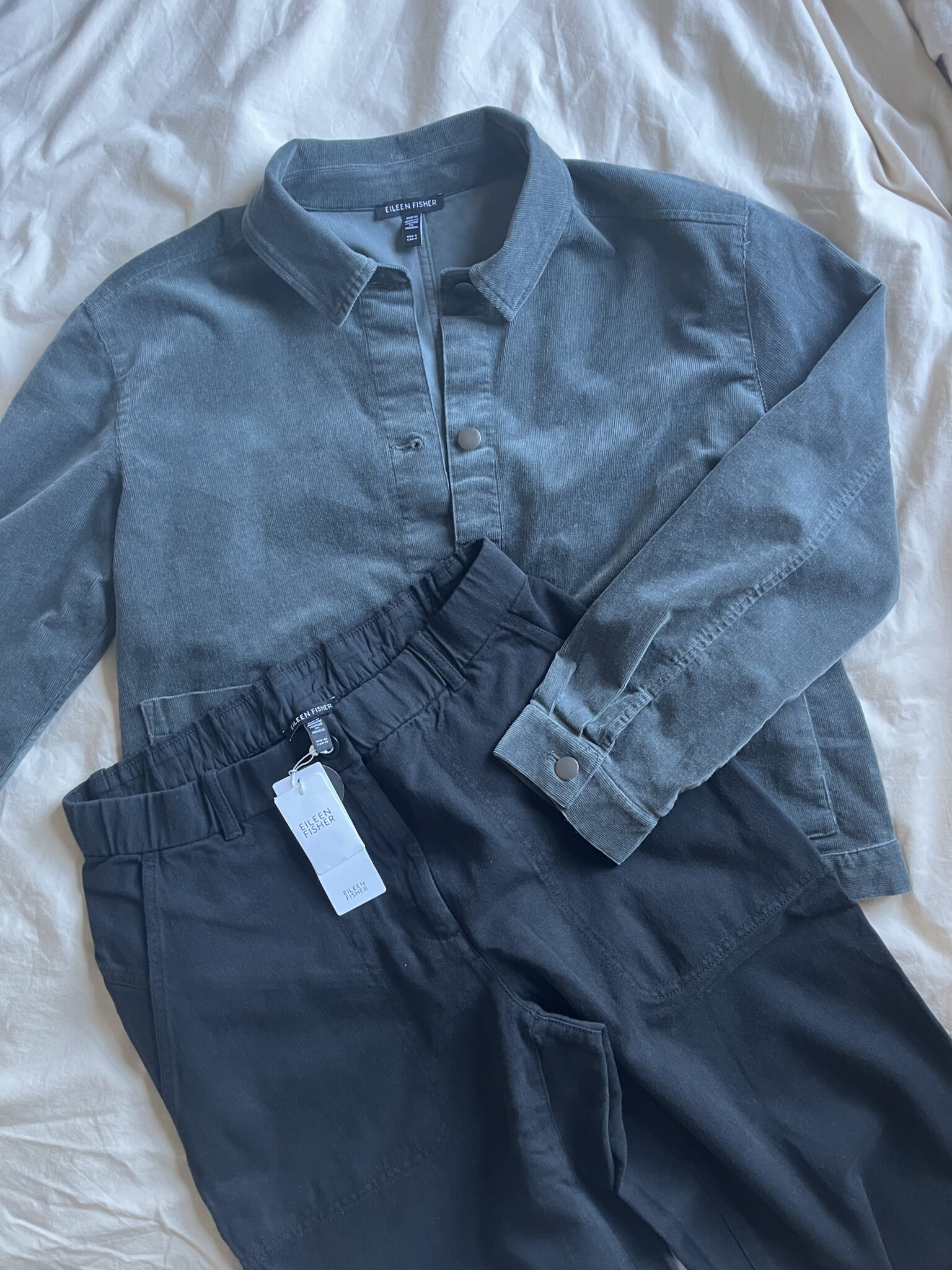 A green collared button-up shirt and a pair of black pants with a white size tag, laid out on a light-colored fabric background.