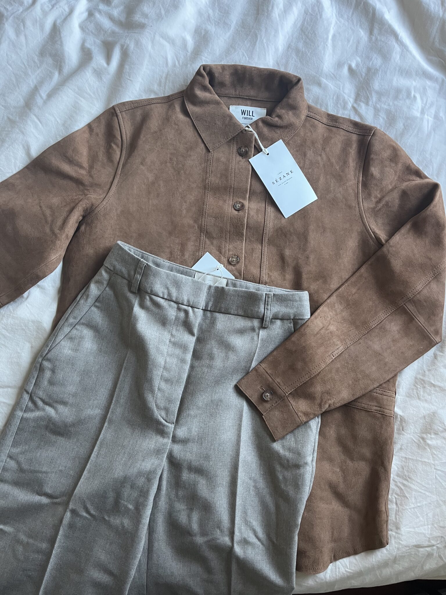 A brown button-up shirt with tags and a pair of light gray dress pants with tags, laid out on a white surface.