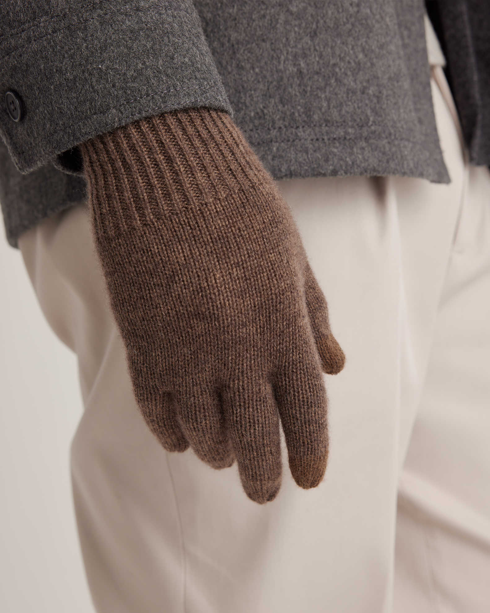 Close-up of a person wearing a gray coat, beige pants, and a brown wool glove.