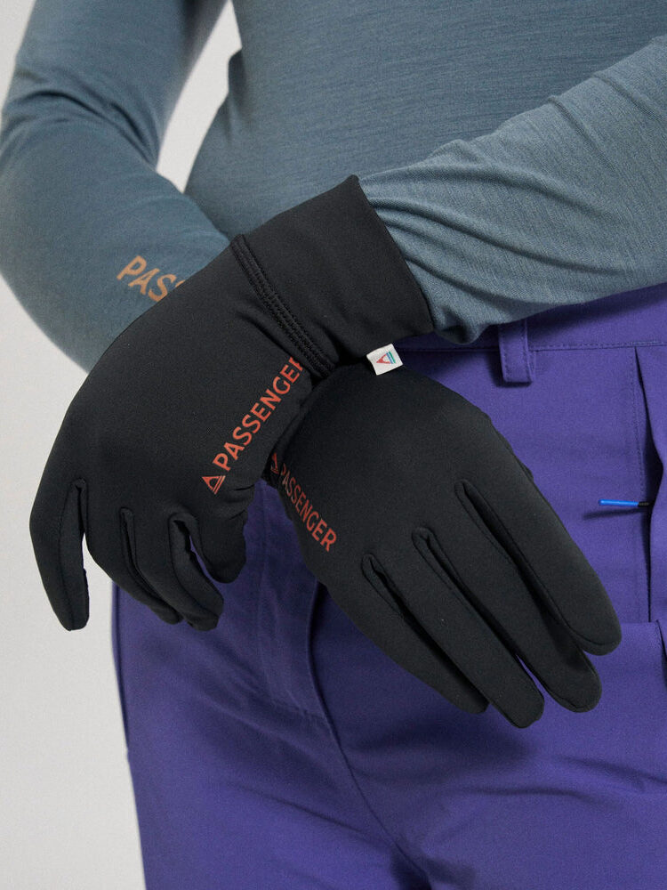 Person wearing black gloves labeled "PASSENGER" and purple pants with a blue pen clipped to the pocket, arms crossed at the waist.