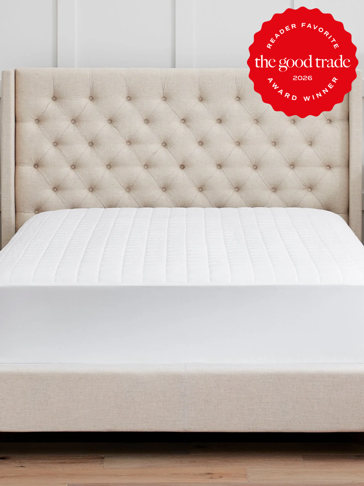 A beige upholstered bed with a tufted headboard and a white quilted mattress. A red award badge in the top right reads “The Good Trade Award Winner 2026 Reader Favorite.”.