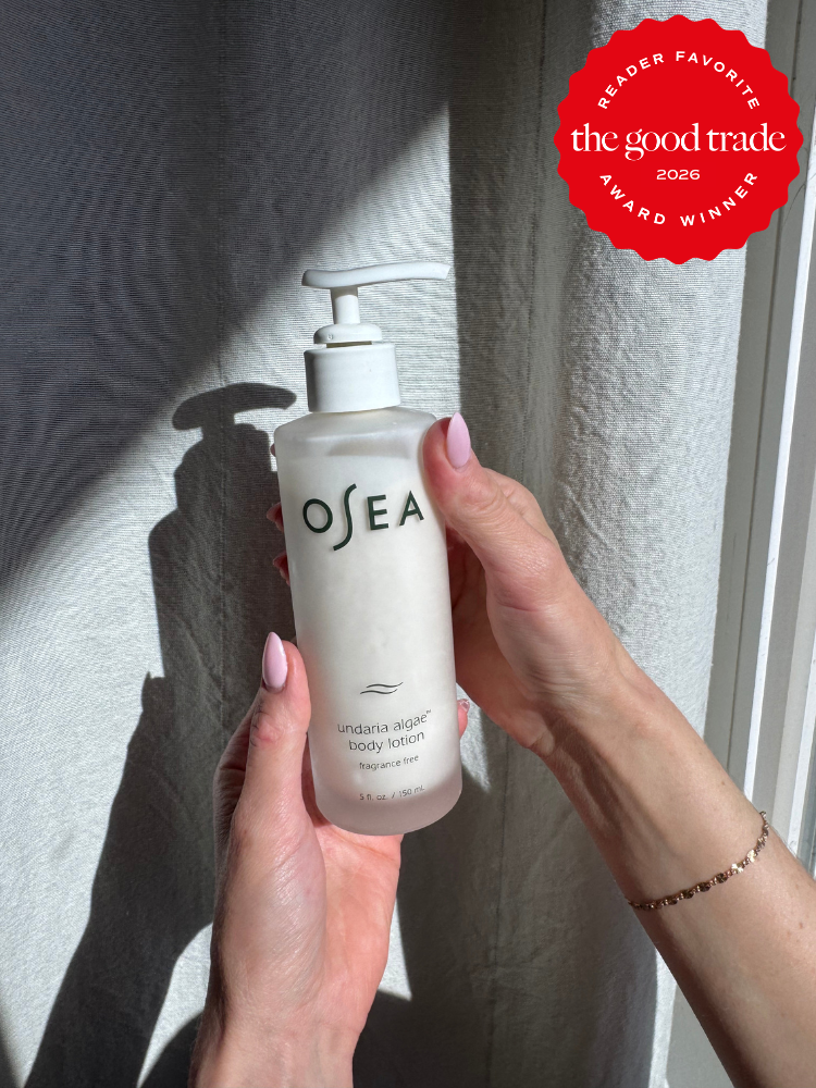 A person holds a bottle of OSEA undaria algae body lotion beside a wall; a red badge in the corner reads “the good trade award winner 2026.”.