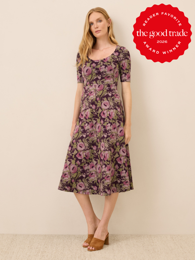 Woman wearing a purple floral dress and brown heeled sandals stands against a beige wall. Red "The Good Trade Reader Favorite 2026 Award Winner" badge in upper right corner.