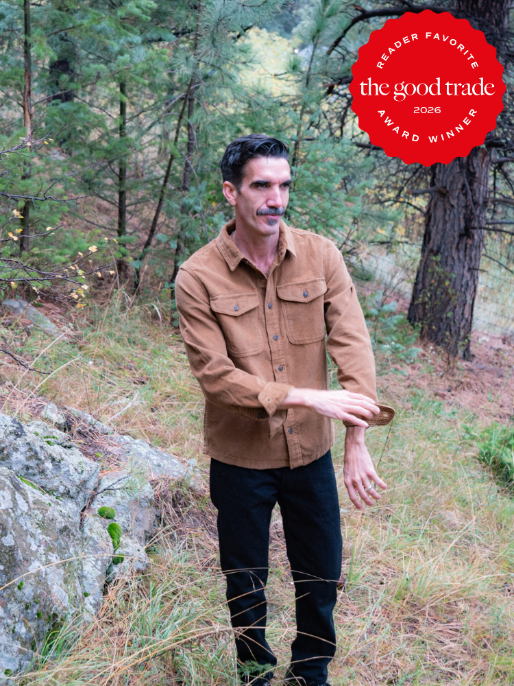 A man in a brown shirt and black pants stands in a forested area. A red badge in the corner reads "The Good Trade Reader Favorite Award Winner 2026.