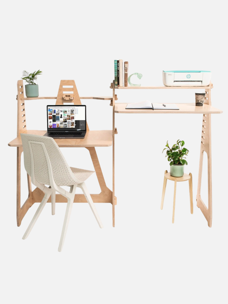 A minimalist home office setup with a wooden desk, laptop, plant, shelf with books and a printer, white chair, and a small side table with a potted plant.